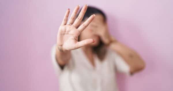 mujer tapándose la cara y con la mano abierta haciendo stop